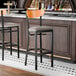 A black metal bar stool with a dark gray vinyl seat and a cherry wood backrest.