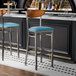 Two Lancaster Table & Seating bar stools with blue seats and antique walnut backs at a black counter.