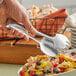 A person holding a pair of American Metalcraft stainless steel tongs over a bowl of salad.