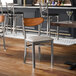 A metal chair with a light gray vinyl seat and an antique walnut wood backrest.