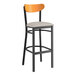 A Lancaster Table & Seating black bar stool with a light gray vinyl seat and cherry wood back.