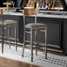 Two Lancaster Table & Seating Boomerang bar stools with a wood back and dark gray vinyl seats at a bar counter.