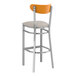 A Lancaster Table & Seating bar stool with a cherry wood back and light gray cushioned seat.