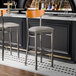 A Lancaster Table & Seating Boomerang bar stool with a light gray vinyl seat and cherry wood back on a counter.