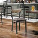 A black metal chair with a dark gray vinyl seat and a driftwood-finished wooden backrest.