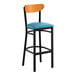 A bar stool with a black metal frame, blue vinyl seat, and a cherry wood backrest.