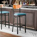 A bar stool with a black metal frame, blue vinyl seat, and cherry wood backrest.