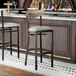 A black bar stool with a light gray vinyl seat and a driftwood-finished wooden backrest.