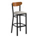 A bar stool with a black metal frame, light gray vinyl seat, and a curved vintage wood backrest.