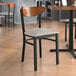 A Lancaster Table & Seating Boomerang Series chair with a wood back, black metal frame, and light gray cushion at a restaurant table.