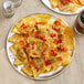 A 10" round aluminum tray of nachos with salsa and cheese on a table in a Mexican restaurant.