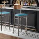 Two Lancaster Table & Seating bar stools with blue vinyl seats at a black counter.