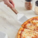 A hand using an American Metalcraft Pie Server with a wood handle to serve pizza.