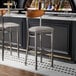 Two Lancaster Table & Seating bar stools with a light gray cushion at a bar counter.
