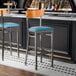 Two Lancaster Table & Seating bar stools with blue seats and cherry wood backs at a black counter.