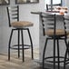 A Lancaster Table & Seating black ladder back swivel bar stool with a taupe vinyl padded seat at a counter.