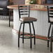A black metal ladder back swivel bar stool with a taupe vinyl padded seat.
