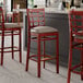 Three Lancaster Table & Seating mahogany wood bar stools with dark gray vinyl seats.