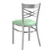 A Lancaster Table & Seating clear coated metal cross back chair with a seafoam vinyl padded seat.