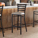 A ladder back bar stool with a distressed copper finish and a light gray vinyl padded seat.