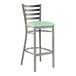 A metal bar stool with a ladder back design and a seafoam green vinyl padded seat.