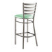 A metal bar stool with a ladder back design and a seafoam green vinyl padded seat.