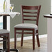 A Lancaster Table & Seating wood restaurant chair with a light gray seat next to a table.