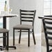 A Lancaster Table & Seating ladder back chair with dark gray vinyl padding on the seat at a table in a restaurant.