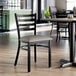 A metal ladder back chair with a dark gray vinyl padded seat and a distressed copper finish.