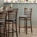 A Lancaster Table & Seating wooden ladder back bar stool with a light gray cushion on the seat at a table in a restaurant.