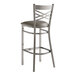 A Lancaster Table & Seating silver metal cross back bar stool with a dark gray vinyl padded seat.