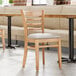 A Lancaster Table & Seating wooden ladder back chair with a light gray vinyl seat.