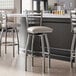 A group of Lancaster Table & Seating clear coat finish ladder back swivel bar stools with light gray padded seats at a bar.