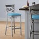 A Lancaster Table & Seating clear coat finish cross back bar stool with a blue vinyl padded seat.