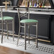 A metal bar stool with a cross back design and a seafoam green vinyl padded seat.