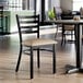 A ladder back chair with a distressed copper finish and a taupe vinyl padded seat.