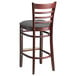 A Lancaster Table & Seating mahogany wood ladder back bar stool with a dark gray vinyl seat.