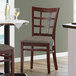 A Lancaster Table & Seating mahogany wood chair with taupe vinyl seat next to a table in a restaurant dining area.