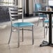 A Lancaster Table & Seating black metal ladder back chair with a blue vinyl cushion on a table.