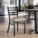 A black ladder back chair with a taupe vinyl padded seat and a detached seat design.