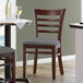 A Lancaster Table & Seating mahogany wood chair with dark gray vinyl seat next to a table.