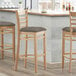 Three Lancaster Table & Seating wooden bar stools with taupe vinyl seats at a counter.