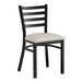 A black Lancaster Table & Seating ladder back chair with a light gray vinyl cushion.