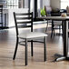A black ladder back chair with a light gray vinyl padded seat.