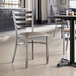 A Lancaster Table & Seating ladder back chair with dark gray vinyl padding on the seat.