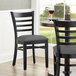 A pair of Lancaster Table & Seating black wood chairs with dark gray vinyl seats at a table in a restaurant.