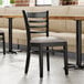 A Lancaster Table & Seating wood ladder back chair with dark gray vinyl seat at a table in a restaurant.