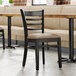 A Lancaster Table & Seating black wood ladder back chair with a taupe vinyl seat next to a table in a restaurant dining area.