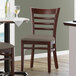 A Lancaster Table & Seating mahogany wood restaurant chair with a taupe vinyl seat next to a table.