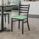 A Lancaster Table & Seating black metal ladder back chair with a seafoam vinyl padded seat.